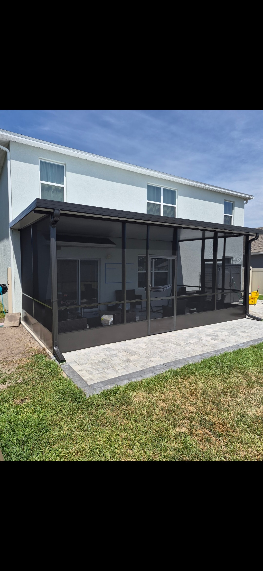 Dark frame screen room enclosure on white two-story home with paver patio