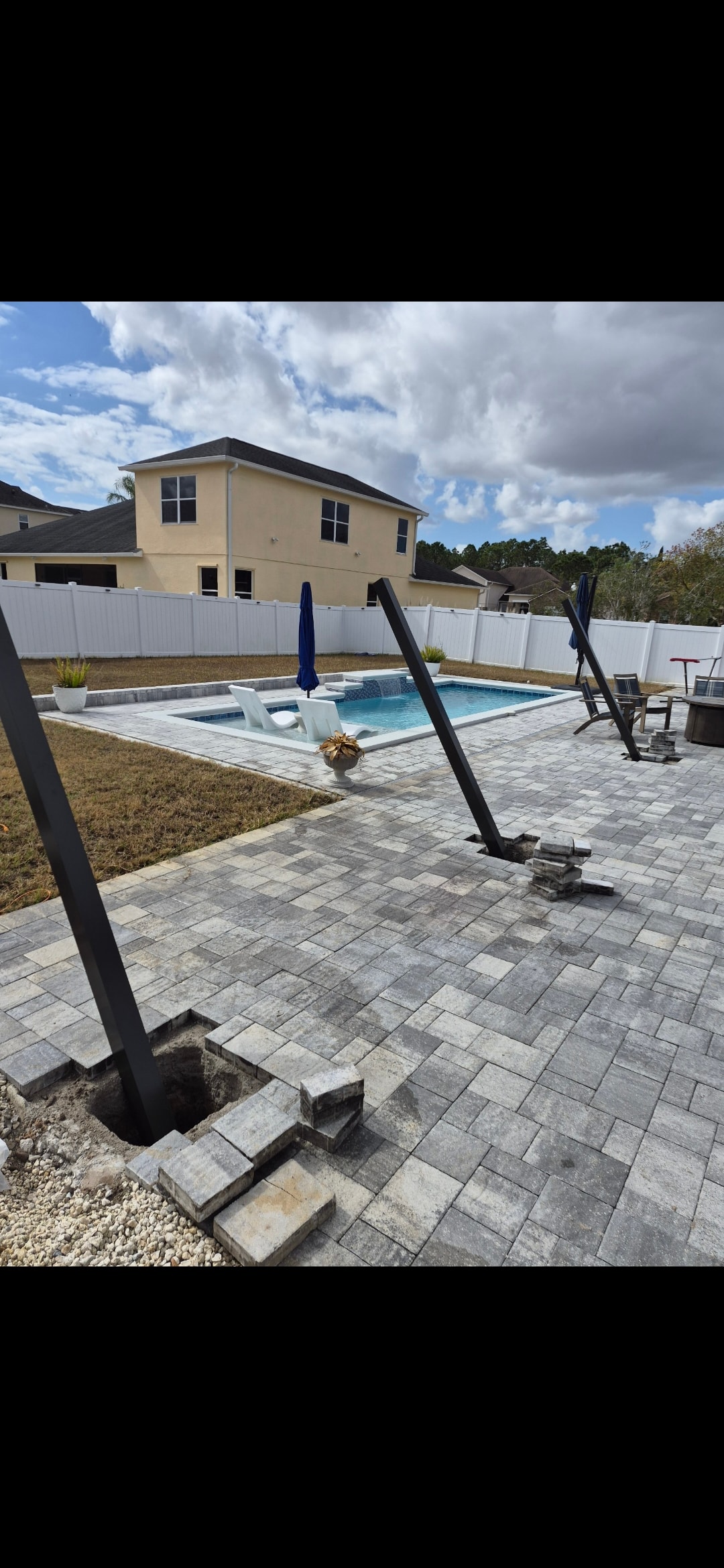 Pool cage frame installation in progress with paver patio and pool