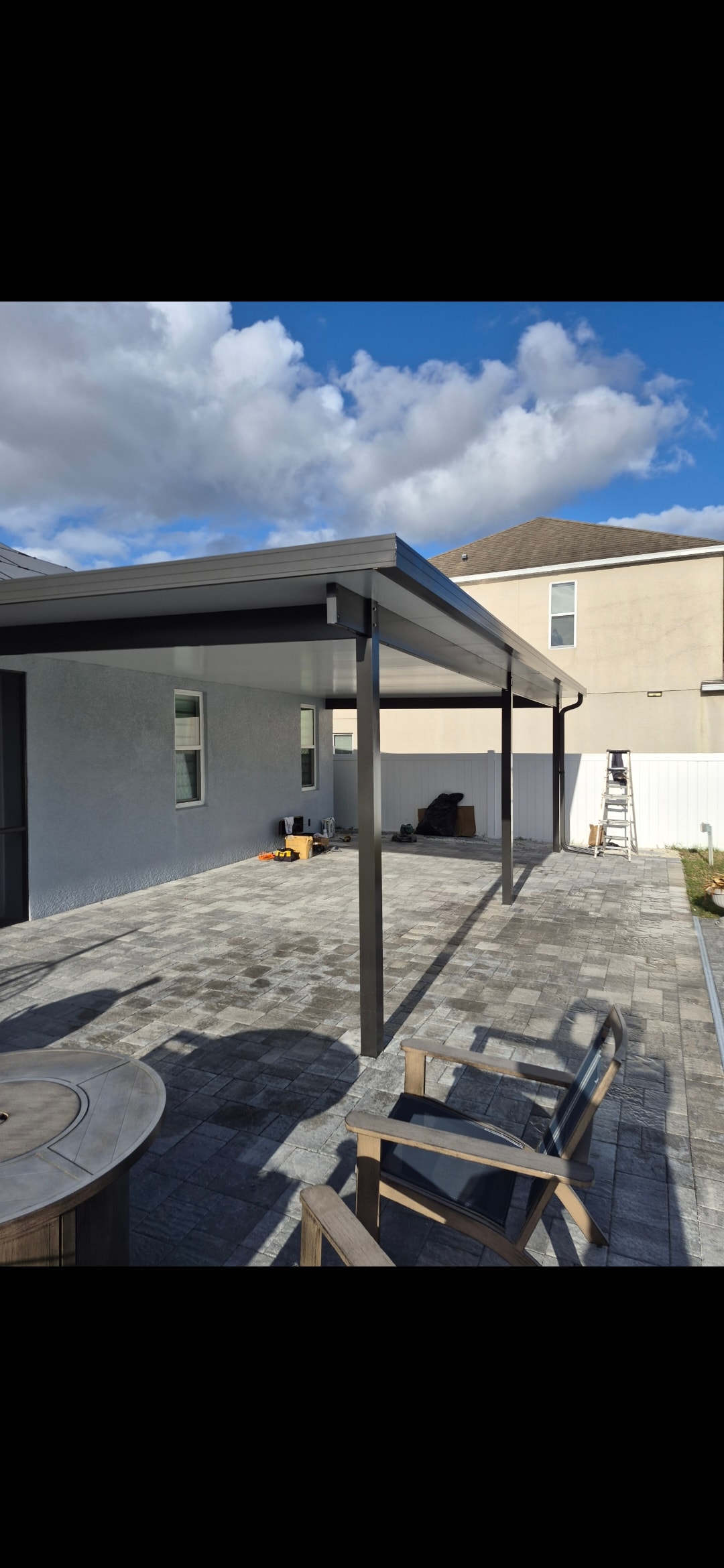 Dark aluminum patio cover installation over paver patio with outdoor seating